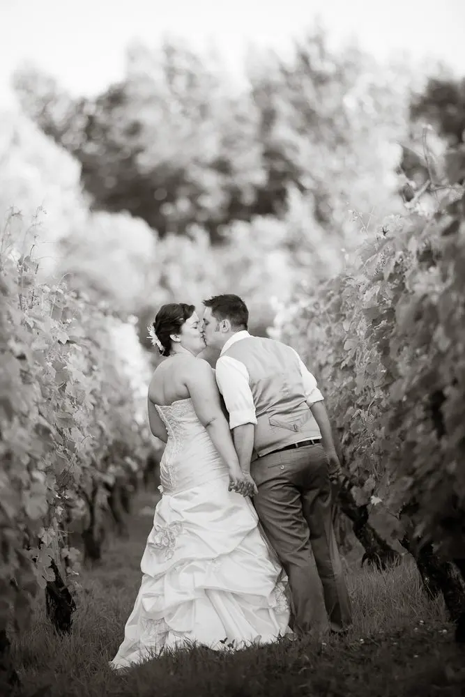bride and groom kissing couple kissing while walking down a vineyard row