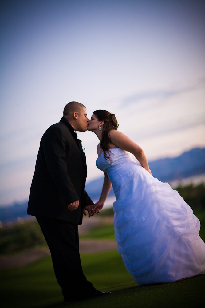 Sunset photograph of bride and groom kissing with golf course and lake in background